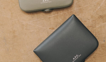 A.P.C. Men's Leather Goods - Beige and charcoal coin wallet on wooden table.