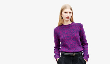 A.P.C. Women's Knitwear & Cardigans - Woman wearing pink sweater and denim skirt standing on balcony.