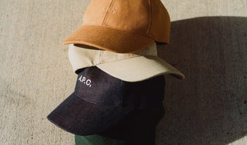 A.P.C. Women's Hats - Stack of baseball caps on concrete back.