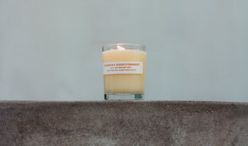 A.P.C. Candles - Lit orange blossom candle on a ledge.