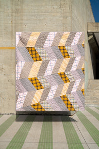 Quilt with geometric pattern displayed against a concrete wall.